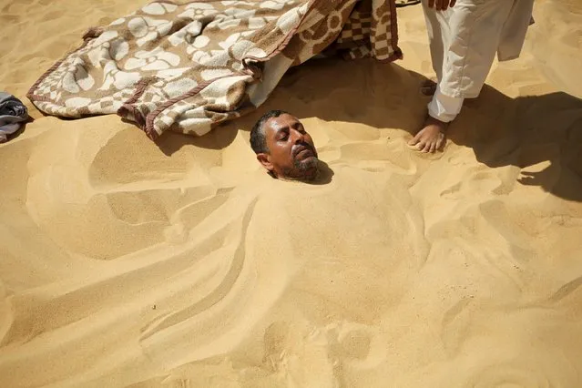 A worker stands next to a patient buried in the hot sand in Siwa, Egypt, August 12, 2015. (Photo by Asmaa Waguih/Reuters)