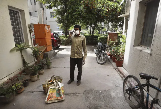 A grocery shop employee, wearing face mask as a precaution against coronavirus, calls a customer living on the second floor to come down to receive their delivery in New Delhi, India, Wednesday, March 25, 2020. The world's largest democracy went under the world's biggest lockdown Wednesday, with India's 1.3 billion people ordered to stay home in a bid to stop the coronavirus pandemic from spreading and overwhelming its fragile health care system as it has done elsewhere. (Photo by Manish Swarup/AP Photo)