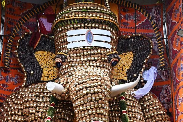 A man (R) removes a cloth to unveil a 30-feet statue of Elephant headed hindu god Ganesha made Metal pots, coconut ,corn and sugarcane at a place worship on Ganesh Chaturthi festival in Chennai on August 31, 2022. (Photo by Arun Sankar/AFP Photo)