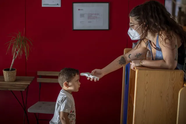 Hugo, 3, has his temperature taken by a teacher as he arrives at Cobi kindergarten in Barcelona, Spain, Friday, June 26, 2020. Spain's cabinet will extend the furlough schemes adopted during the coronavirus lockdown that brought the economy to a standstill until the end of September. (Photo by Emilio Morenatti/AP Photo)
