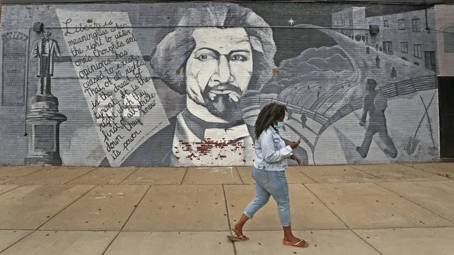 A woman, wearing a protective mask due to the COVID-19 virus outbreak, walks past a mural in tribute to Frederick Douglass on Wednesday, June 24, 2020, in the South End neighborhood of Boston. (Photo by Charles Krupa/AP Photo)