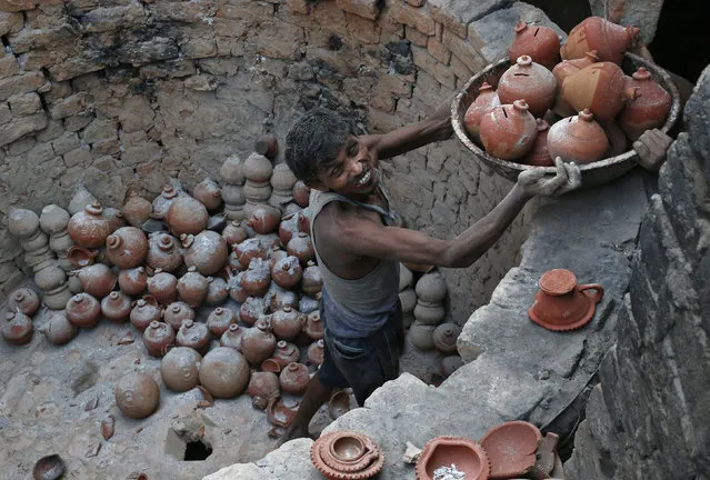 A potter carries a basket filled with clay money boxes at a workshop ahead of the Hindu festival of Diwali in New Delhi October 16, 2014. Earthen goods are sold in large numbers during Diwali, the annual Hindu festival of lights, as people use them to decorate their homes. The Diwali festival will be observed this year on October 23. (Photo by Anindito Mukherjee/Reuters)