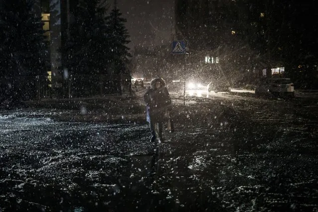 A woman crosses the street during snowfall, as power outages continue in Kyiv, Ukraine, Friday, December 16, 2022. Ukrainian authorities reported explosions in at least three cities Friday, saying Russia has launched a major missile attack on energy facilities and infrastructure. (Photo by Felipe Dana/AP Photo)