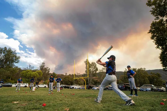 Little League players warm-up before a game as a brush fire is ablaze in back at a field next to the Sycuan Casino on the Sycuan Indian reservation during the Valley Fire, near Dehesa, in San Diego, California on September 6, 2020. The Valley Fire in the Japatul Valley burned 4,000 acres overnight with no containment and 10 structures destroyed, Cal Fire San Diego said. (Photo by Sandy Huffaker/AFP Photo)