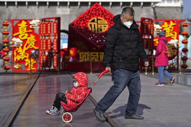 A man pulls a child past a Lunar New Year decoration on display at the Qianmen pedestrian shopping street, a popular tourist spot in Beijing, Tuesday, January 17, 2023. China has announced its first population decline in decades as what has been the world's most populous nation ages and its birthrate plunges. (Photo by Andy Wong/AP Photo)
