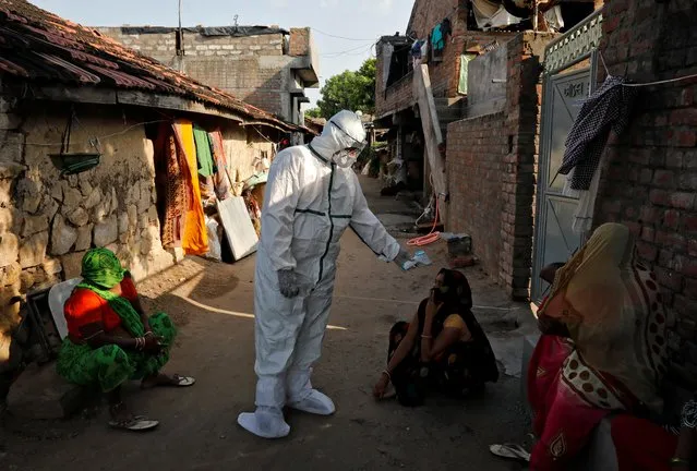 A healthcare worker wearing personal protective equipment (PPE) checks the temperature of a woman sitting outside her house in an alley during a door-to-door survey for the coronavirus disease (COVID-19), in Jakhan village in the western state of Gujarat, India, September 22, 2020. (Photo by Amit Dave/Reuters)