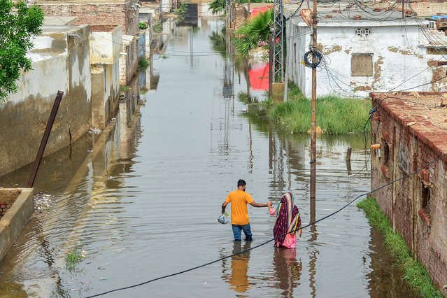 People wade through a flooded street in a residential area following heavy monsoon rains in Hyderabad, in Sindh province, on July 15, 2025. (Photo by Akram Shahid/AFP Photo)