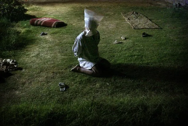 A detained Iraqi man with a plastic bag covering his head sits in garden of a house searched by U.S. soldiers during a night raid in Tikrit, October 30, 2003. (Photo by Damir Sagolj/Reuters)