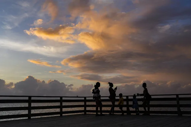 People take photos from the seawall at sunset in Georgetown, Guyana, Wednesday, April 19, 2023. In 2009 Norway signed a deal to provide $250 million in funding to ensure that Guyana's 18 million hectares of forest remain intact. (Photo by Matias Delacroix/AP Photo)