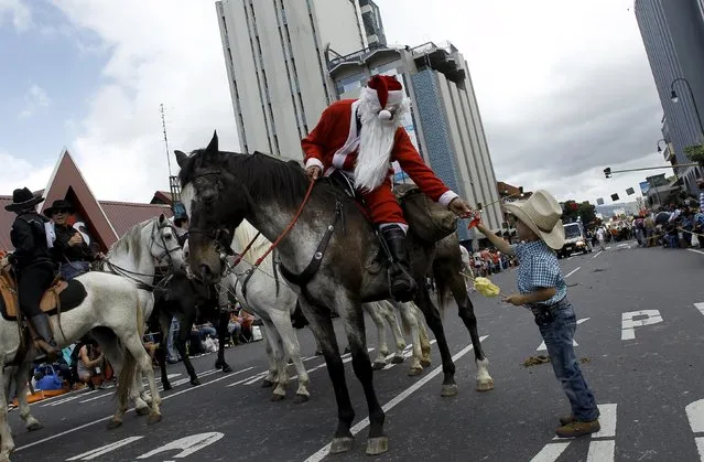 A rider dressed as Santa Claus gives a toy to a boy during a parade on horses through the streets of San Jose, Costa Rica December 26, 2015.Thousands of riders participated in the parade, which is part of annual year-end festivities. (Photo by Juan Carlos Ulate/Reuters)