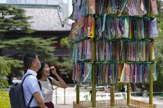 Visitors watch paper strips with others' wishes written on them for the Star Festival, or “tanabata”, to a bamboo branch at Zojoji temple Friday, July 7, 2023, in Tokyo, Japan. According to legend, deities "Orihime" (Vega) and her lover “Hikoboshi” (Altair), separated by the Milky Way, are allowed to meet only once a year during this period. People celebrate the festival by writing wishes on strips of paper and hanging them under bamboo trees. (Photo by Shuji Kajiyama/AP Photo)