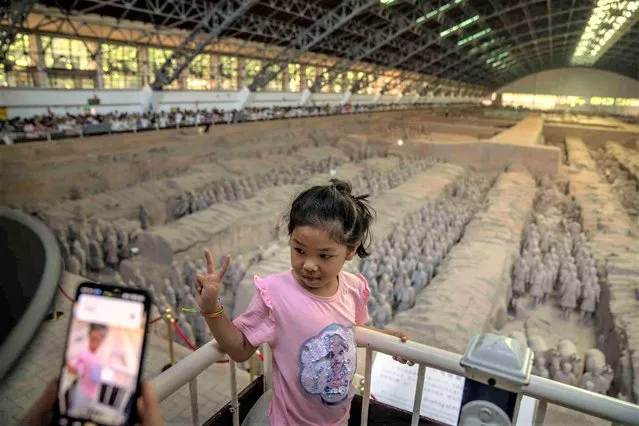 A girl poses for a photo in front of excavated figures on display at the Museum of Terracotta Warriors and Horses of Emperor Qin Shihuang in Xi'an in northwestern China's Shaanxi Province, Sunday, July 16, 2023. (Photo by Mark Schiefelbein/AP Photo)