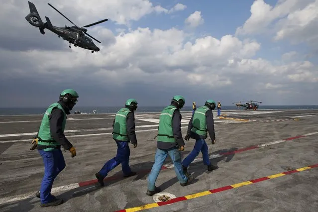 Crew walk on the flight deck of France's Charles de Gaulle aircraft carrier as an helicopter flies overhead in the Gulf, January 29, 2016. (Photo by Philippe Wojazer/Reuters)