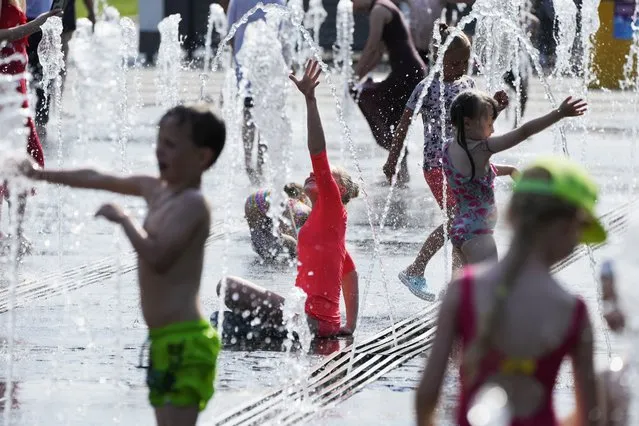 Children play in a fountain at a park next to an embankment of the Moscow River in Moscow, Russia, Wednesday, June 23, 2021. The hot weather in Moscow is continuing with temperatures reach 36 degrees Celsius during a day. (96,8 Fahrenheit). (Photo by Pavel Golovkin/AP Photo)