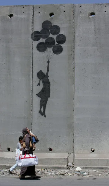 A Palestinian woman and her children walk past a Banksy drawing on the controversial Israeli barrier in the West Bank city of Aram in 2005. (Photo by Ammar Awad/Reuters)