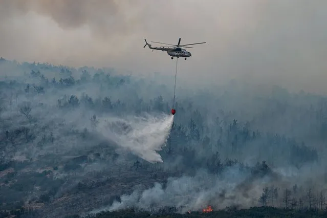 A helicopter drops water on a wildfire on an area near the village of Ikizce, in the Mugla province, on August 6, 2021. (Photo by Yasin Akgul/AFP Photo)