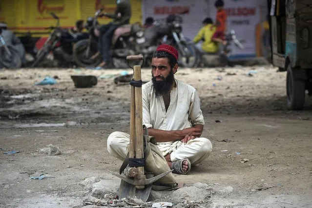 A daily wage labourer sits along a road waiting for customers to hire him for a day job in Karachi on July 25, 2021. (Photo by Rizwan Tabassum/AFP Photo)