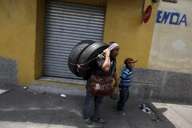 A man carries two tires with his head and waits for the public bus with a child on the streets of Guatemala City, April 9, 2015. (Photo by Jorge Dan Lopez/Reuters)