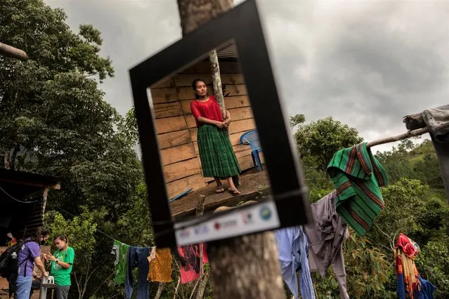 Irma Cal Pop, 26, is reflected in a mirror donated by USAID while members of the CrossPoint Baptist Church of Alabama, help to install an energy saving kitchen in her home, in the makeshift settlement Nuevo Queja, Guatemala, Monday, July 12, 2021. Mirrors donated by USAID hang inside every ramshackle home of the makeshift settlement. (Photo by Rodrigo Abd/AP Photo)
