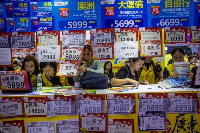 In this March 3, 2018, photo, people check on travel packages offered by travel agencies during the Guangzhou International Travel Fair in Guangzhou in south China's Guangdong province. Travelers in China were blocked from buying plane tickets 17.5 million times last year as a penalty for failing to pay fines or other offenses. The Chinese government reported this week on penalties imposed under a controversial “social credit” system the ruling Communist Party says will improve public behavior. (Photo by Chinatopix via AP Photo)