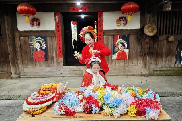A villager pins a flowery headwear for a tourist at Xunpu Village on January 27, 2024 in Fuzhou, Fujian Province of China. Xunpu flowery headwear, dubbed 'overhead gardens', have been a signature of “Xunpu Women Customs” listed as a national intangible heritage in 2008. They attracted millions of eyes in the cyber world in early 2023, followed by a sustainable tourist boom in the village, where visitors are able to literally fit their heads in them. (Photo by Wang Dongming/China News Service/VCG via Getty Images)