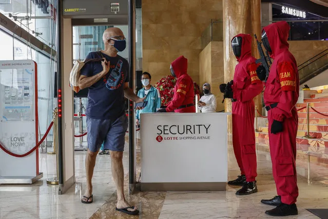 A visitor walks through a check point as mall security guards dressed in the Netflix series Squid Game costumes look on at Lotte Shopping Avenue in Jakarta, Indonesia, 20 October 2021. The popular Korean series was taken as the theme as part of the Halloween celebrations. (Photo by Mast Irham/EPA/EFE)