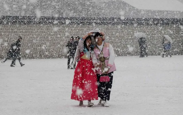 A couple wearing South Korea's traditional costume “Hanbok” shares a jacket to protect themselves from heavy snow at the 14th-century Gyeongbok Palace, one of South Korea's well known landmarks in Seoul, South Korea, Sunday, February 28, 2016. (Photo by Ahn Young-joon/AP Photo)