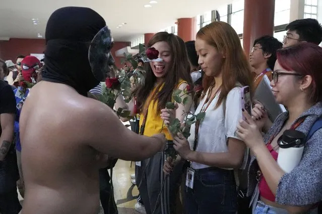 A masked fraternity student from the University of the Philippines gives roses during their annual naked run dubbed “Oblation Run” Friday, February 16, 2024 in Quezon city, Philippines. About a dozen male students made the traditional run to show disdain on some lawmakers who plan to change parts of the constitution. (Photo by Aaron Favila/AP Photo)