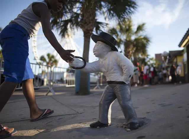 A boy touches an old lawn jockey that has been painted white on Ocean Boulevard during the 2015 Atlantic Beach Memorial Day BikeFest in Myrtle Beach, South Carolina May 24, 2015. (Photo by Randall Hill/Reuters)