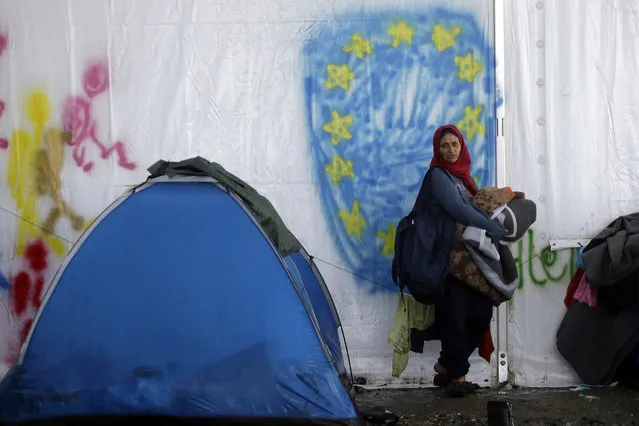 A woman standing in front of a graffiti depicting the EU flag, holds her blankets at the end of a rainstorm at the northern Greek border point of Idomeni, Greece, Sunday, April 24, 2016. Many thousands of migrants remain at the Greek border with Macedonia, hoping that the border crossing will reopen, allowing them to move north into central Europe. (Photo by Gregorio Borgia/AP Photo)