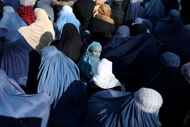 A girl sits in front of a bakery in the crowd with Afghan women waiting to receive bread in Kabul, Afghanistan, January 31, 2022. (Photo by Ali Khara/Reuters)