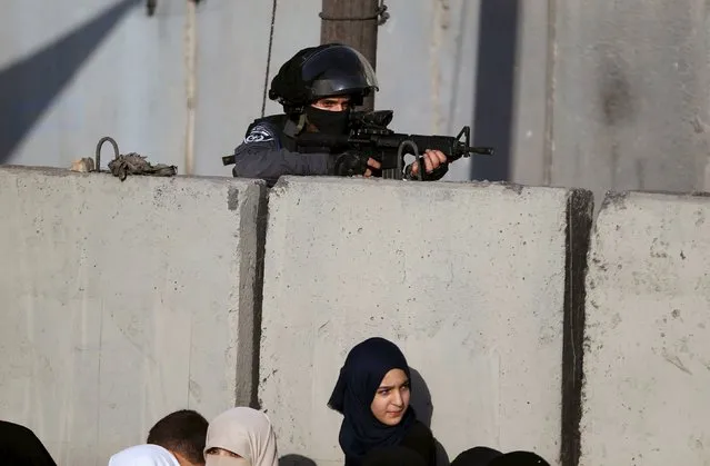 An Israeli border policeman keeps guard as a Palestinian girl waits with her mother to show their permits to Israeli security officers to make their way to attend the third Friday prayer of Ramadan in Jerusalem's al-Aqsa mosque, at Qalandia checkpoint near the West Bank city of Ramallah, July 3, 2015. (Photo by Mohamad Torokman/Reuters)