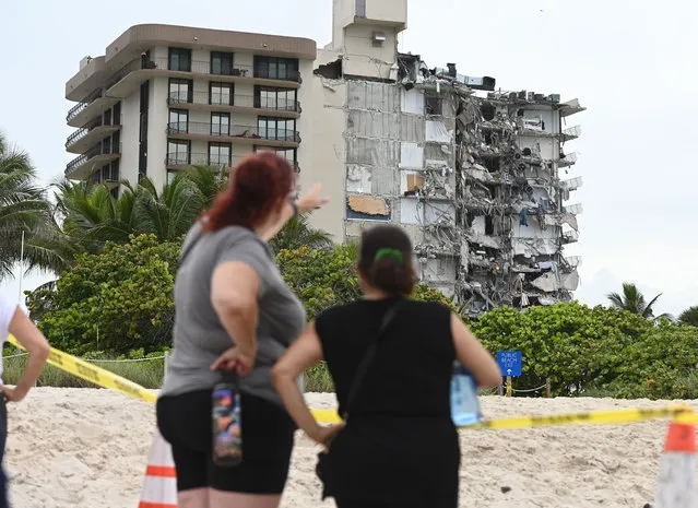 Bystanders look at the partially collapsed Champlain Towers in the community of Surfside outside Miami, Florida on June 25, 2021. Miami-Dade Fire Rescue officials said more than 80 units responded to the collapse at the condominium building near 88th Street and Collins Avenue just north of Miami Beach on last 24 June around at 2 a.m. Rescue services are still searching for people under the rubble. (Photo by Larry Marano/Rex Features/Shutterstock)
