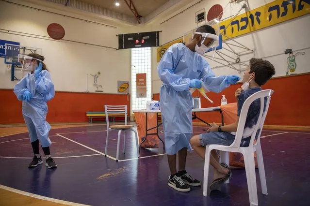 A Medical worker tests an Israeli boy for the coronavirus at a basketball court turned into a coronavirus testing center, in Binyamina, Israel, Tuesday, June 29, 2021. Israel's prime minister is urging the country's youth to get vaccinated as coronavirus case numbers have crept up in recent days due to a localized outbreak of the Delta variant. (Photo by Ariel Schalit/AP Photo)
