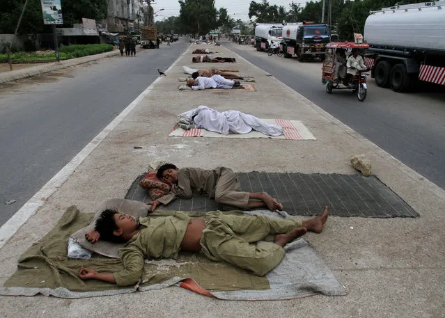 A three-wheeled tuk-tuk moves past homeless people sleeping in the middle of a road early on the morning on Wednesday, July 8, 2015 in Karachi, Pakistan. (Photo by Fareed Khan/AP Photo)