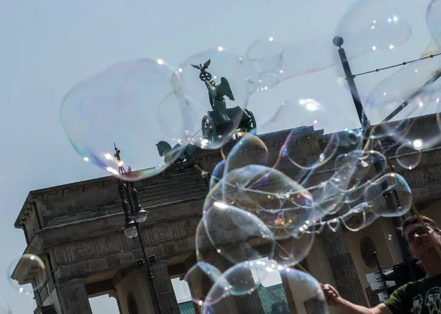 Bubbles float at the Brandenburg Gate in Berlin, Germany, 23 May 2016. A Polish street artist sends the partly giant bubbles into the blue sky. (Photo by Paul Zinken/EPA)
