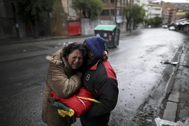 A couple, holding a Bolivian flag, embrace after spending the night celebrating the resignation of President Evo Morales in La Paz, Bolivia, Monday, November 11, 2019. Morales resigned Sunday under mounting pressure from the military and the public after his re-election victory triggered weeks of fraud allegations and deadly protests. (Photo by Natacha Pisarenko/AP Photo)