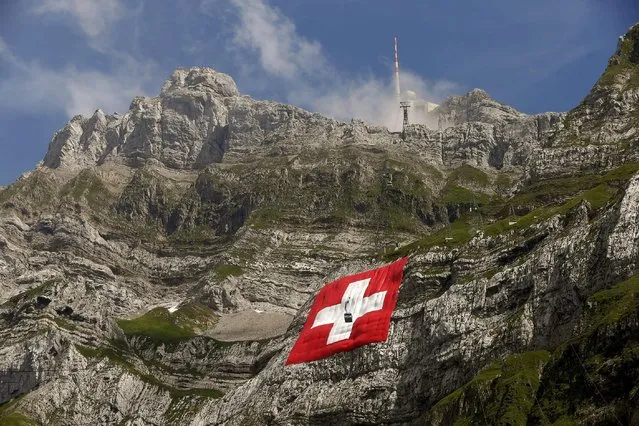 A cablecar descents in front of a huge 80x80 metres (262x262 feet) Swiss national flag on the western face of the north-eastern Swiss landmark Mount Saentis, Switzerland July 31, 2015. The flag marks the Swiss National Day. (Photo by Arnd Wiegmann/Reuters)