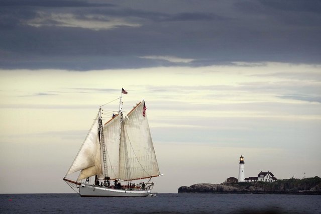 The schooner Timberwind cruises with her guests on a sunset sail off the coast of Cape Elizabeth, Maine, Thursday, June 8, 2023. Portland Head Light stands at the mouth of the harbor in the background. While much of the East Coast is dealing with the smoke from the Canadian wildfires, Maine has been enjoying clean air due to a low pressure system and favorable winds. (Photo by Robert F. Bukaty/AP Photo)