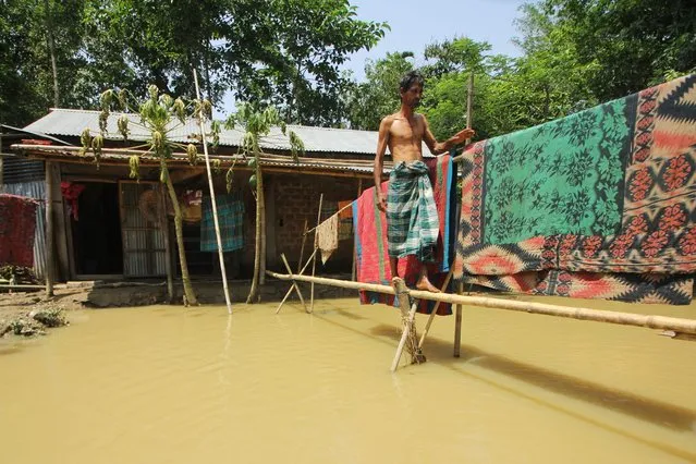 A man walks across makeshift foot bridge made of bamboo outside his home on a flooded area following heavy rains in Sylhet on May 24, 2022. At least four million people have been affected by the worst floods in Bangladesh's northeast for nearly two decades, the United Nations said on May 23. (Photo by Mamun Hossain/AFP)