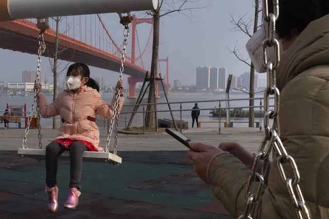 A girl wears a face mask as she play on a swing near the Yingwuzhou Yangtze River Bridge in Wuhan in central China's Hubei Province, Wednesday, January 29, 2020. Countries began evacuating their citizens Wednesday from the Chinese city hardest-hit by a new virus that has now infected more people in China than were sickened in the country by SARS. (Photo by Arek Rataj/AP Photo)