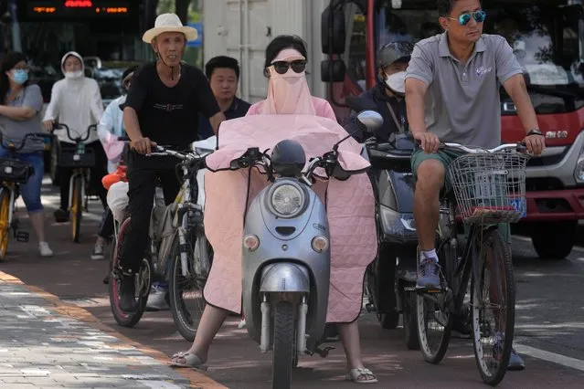 A woman covered up from the sun waits at a traffic junction, Wednesday, July 13, 2022, in Beijing. (Photo by Ng Han Guan/AP Photo)
