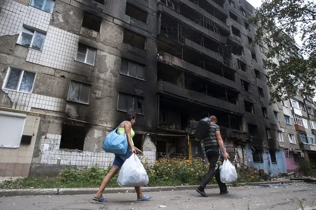 Local residents walk past a damaged building after shelling, during a fighting between pro-Russian rebels and Ukrainian government forces in Shakhtarsk, Donetsk region, eastern Ukraine, Thursday, August 7, 2014. (Photo by Evgeniy Maloletka/AP Photo)
