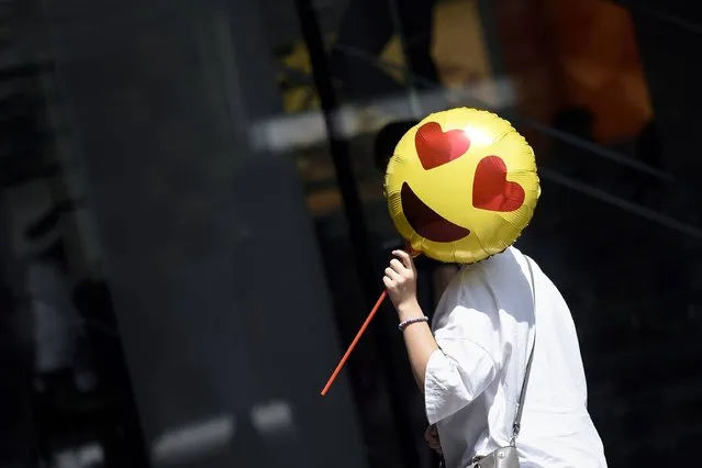 A woman holds a balloon as she walks past a store on Chinese Valentine's Day in Beijing on August 28, 2017. Qixi Festival, or Chinese Valentine's Day, which falls on the seventh day of the seventh lunar month, is a time when girls traditionally demonstrate their domestic skills and wish for a good husband. (Photo by Wang Zhao/AFP Photo)