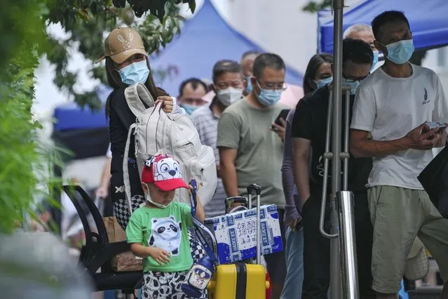 A woman and a child with their luggage stand watch as masked residents line up to get their routine COVID-19 throat swab at a coronavirus testing site in Beijing, Wednesday, August 3, 2022. (Photo by Andy Wong/AP Photo)