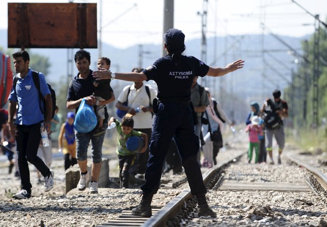 A Greek police officer guides migrants arriving to enter Macedonia, near border with Greece, August 27, 2015. Migrants are trekking from the southern Macedonian border near Gevhelija to the northern border with Serbia on their way to Western Europe. (Photo by Ognen Teofilovski/Reuters)
