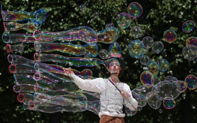 A street artiste blows bubbles during a performance on a street in Paris on June 17, 2022, as a heatwave sweeps across much of France and Europe. French officials have urged caution as a record pre-summer heatwave spread across the country from Spain, where authorities were fighting forest fires on a sixth day of sweltering temperatures. The Meteo France weather service said it was the earliest hot spell ever to hit the country, worsening a drought caused by an unusually dry winter and spring, and raising the risk of wildfires. (Photo by Stefano Rellandini/AFP Photo)