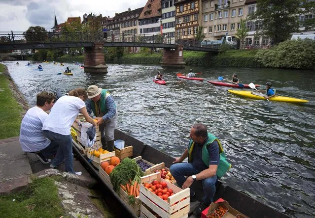 Greengrocer Christophe Moegling (L) and an employee (R) sell fruits and vegetables from a boat on a canal in Strasbourg, eastern France, on September 6, 2017. Three times a week, fruits and vegetables, harvested from an urban farm in the suburbs of Strasbourg, are sold at several stops along the Ill river. (Photo by Patrick Hertzog/AFP Photo)