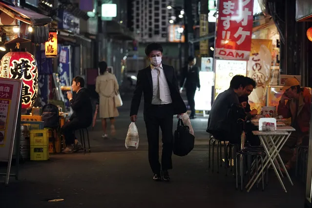 In this April 28, 2020, file photo, a man wearing a face mask against the spread of the new coronavirus walks through a bar street in Tokyo. Under Japan's coronavirus state of emergency, people have been asked to stay home. Many are not. Some still have to commute to their jobs despite risks of infection, while others are dining out, picnicking in parks and crowding into grocery stores with scant regard for social distancing. (Photo by Eugene Hoshiko/AP Photo)