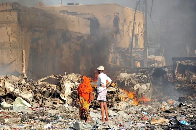 A man and woman look at the damages on the site of the explosion of a truck bomb in the centre of Mogadishu, on October 14, 2017. (Photo by Mohamed Abdiwahab/AFP Photo)
